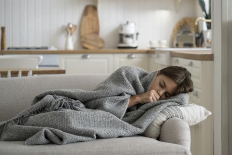Mujer tumbada en el sofá tapada con manta que sufre escalofríos sin fiebre.